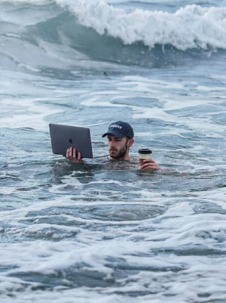 A man working on a laptop while standing in ocean waves.